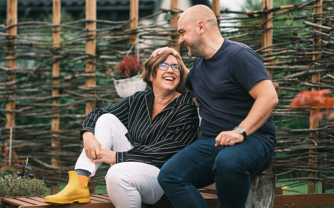 De två förläggarna på Eget Förlag (Helene Engström och Joakim Hedström) sitter i en trädgård framför en flätad pilvägg. Joakim har sin hand på Helenes huvud. Foto av Crelle.